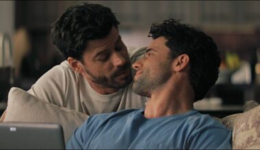 From left to right: Scott leaning against the back of the couch and looking at Kip who is sitting on the couch and looking up at Scott.