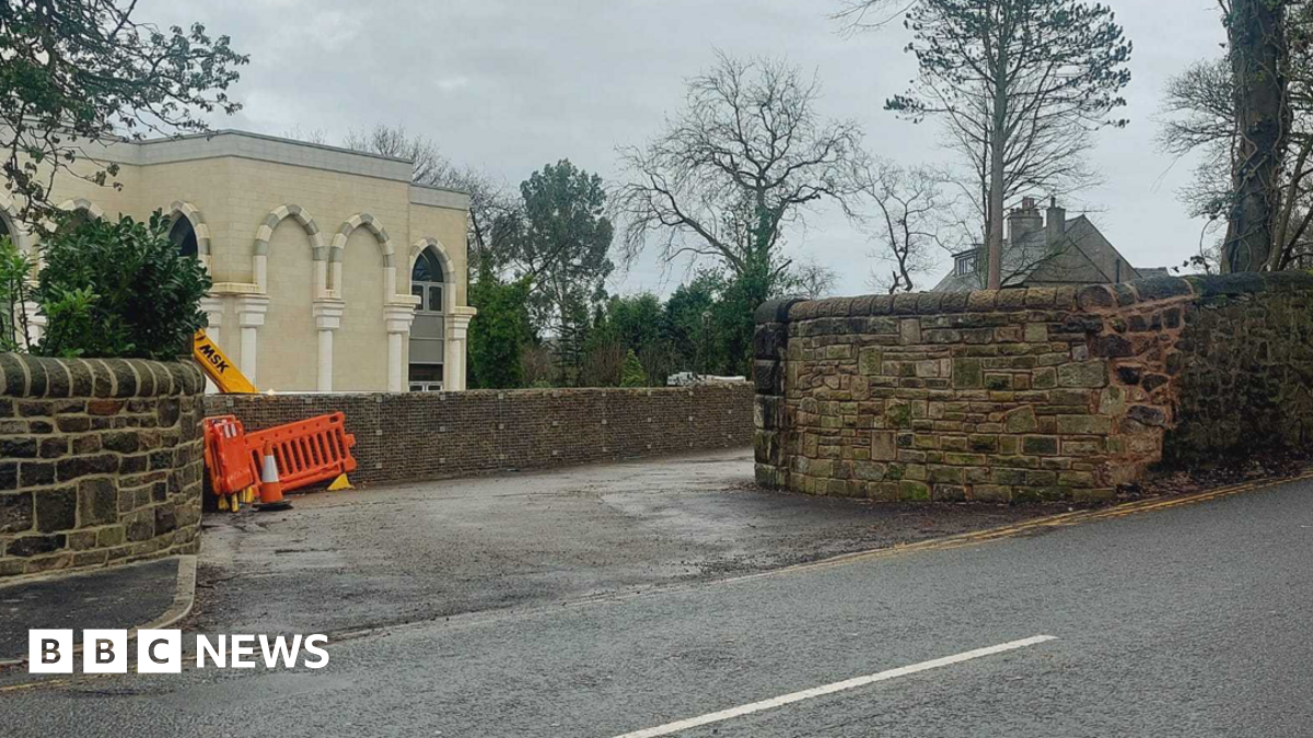 The stone entrance to the Issa brother's mosque with a white building behind it and an orange work fence