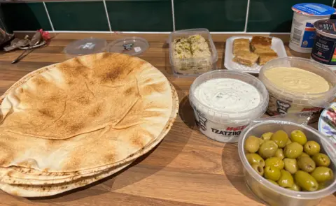 Olives, tzatziki, hummus, pitta, baklava on a wooden surface
