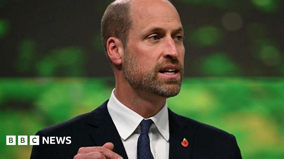 Prince William in a dark suit, white shirt and dark tie. He has a red poppy pin on his lapel.