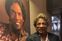 Kamahl standing in front of 1970s poster of himself at the Opera House