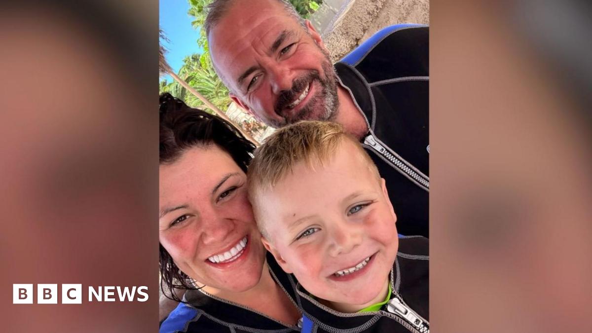Giselle, a woman with dark hair, Charlie a man with grey hair and a beard and a young Hendrix who has light hair, they all have bright smiles while on holiday wearing wetsuits.
