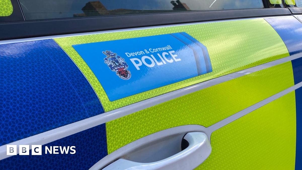 The side of a blue and yellow police vehicle. 'Devon and Cornwall Police' is written in a blue box on one of the doors of the car.