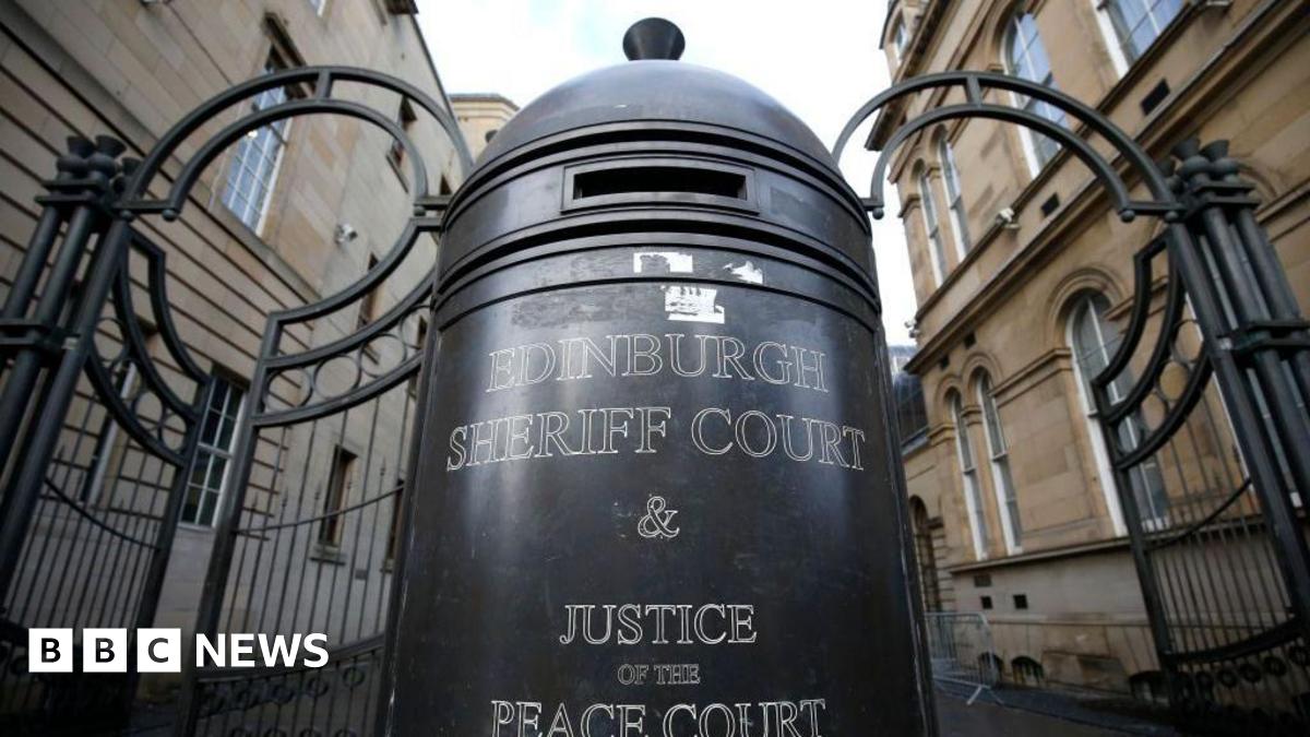 The black gates at the entrance of Edinburgh Sheriff Court. In the centre is a large bollard which has white print reading "Edinburgh Sheriff Court and Justice of the Peace Court".