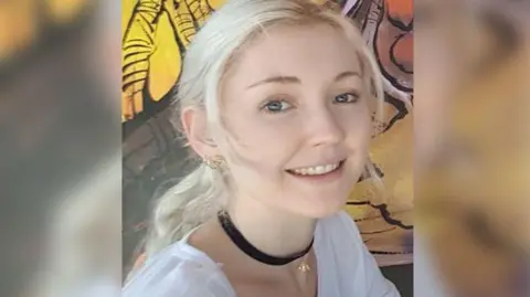 Queensland Police Service A close-up image of a woman with blonde hair and blue eyes smiling at the camera.