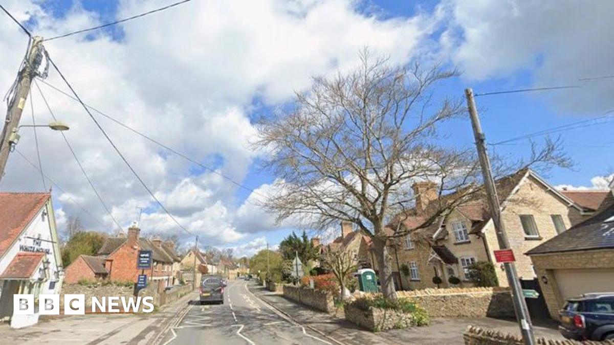 Road through a village with a white pub on the left and homes to the right.