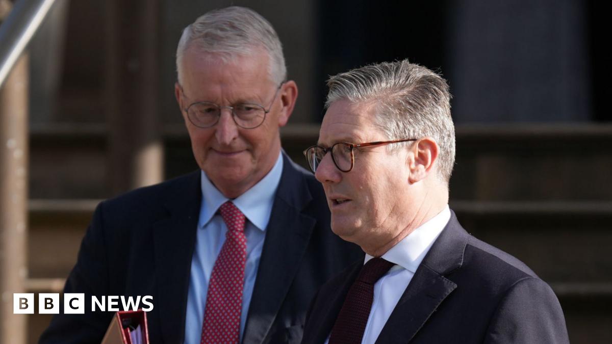 The head and shoulders of Hilary Benn, wearing thin rimmed glasses and a dark suit with a white shirt.