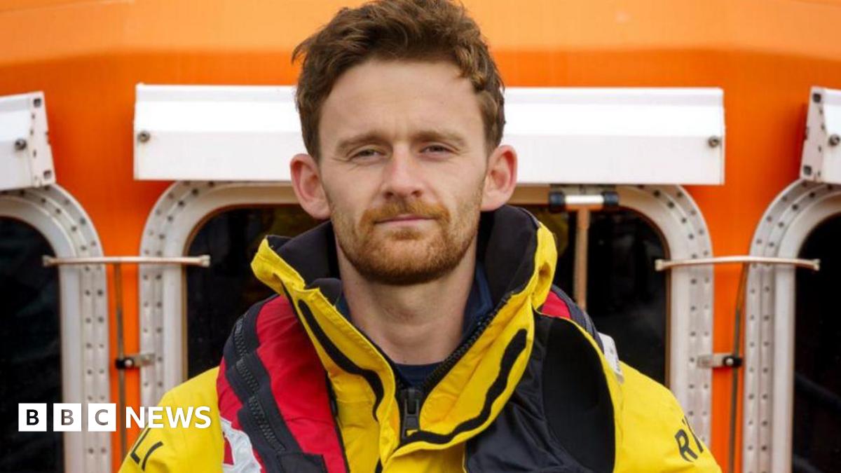 A man with ginger-coloured hair and beard wearing a yellow coat and a red life jacket.