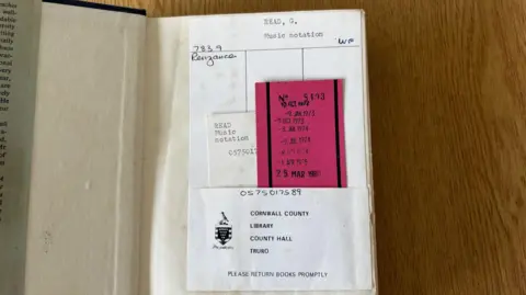 Cornwall Council An open book with the words 'Read, G, Music notation' written. There is a list of dates which date back to 1973 of when it was taken out. It also says 'Cornwall County Library, County Hall, Truro. Please return books promptly'. 