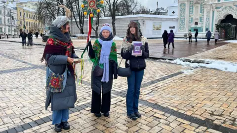 Three teenage girls singing carols in folk-style clothes