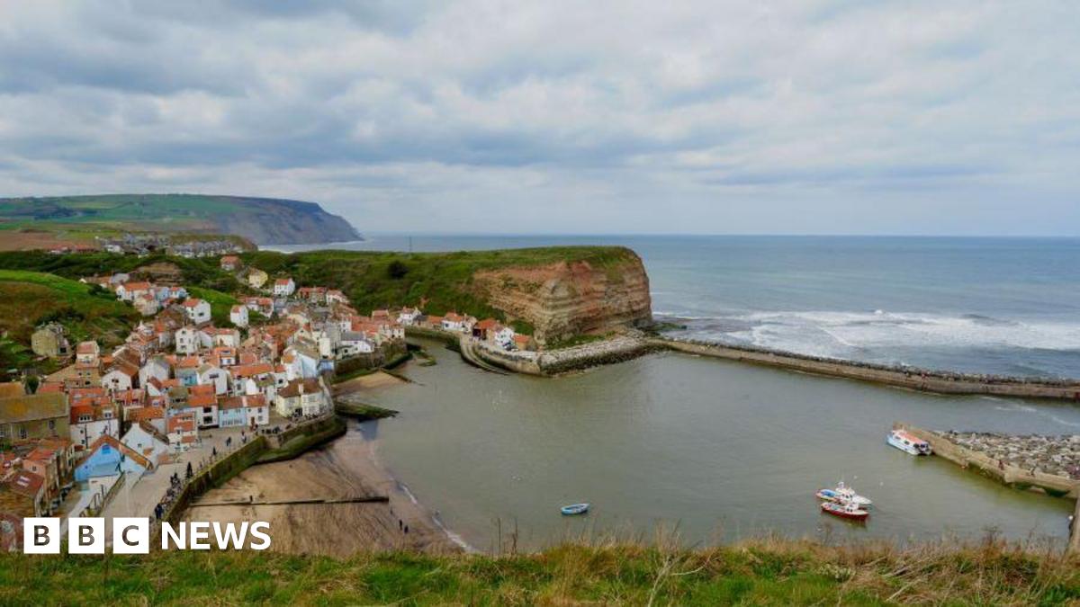 An aerial view of the village of Staithes which shows the pier stretching out into the sea to the right of the image.
