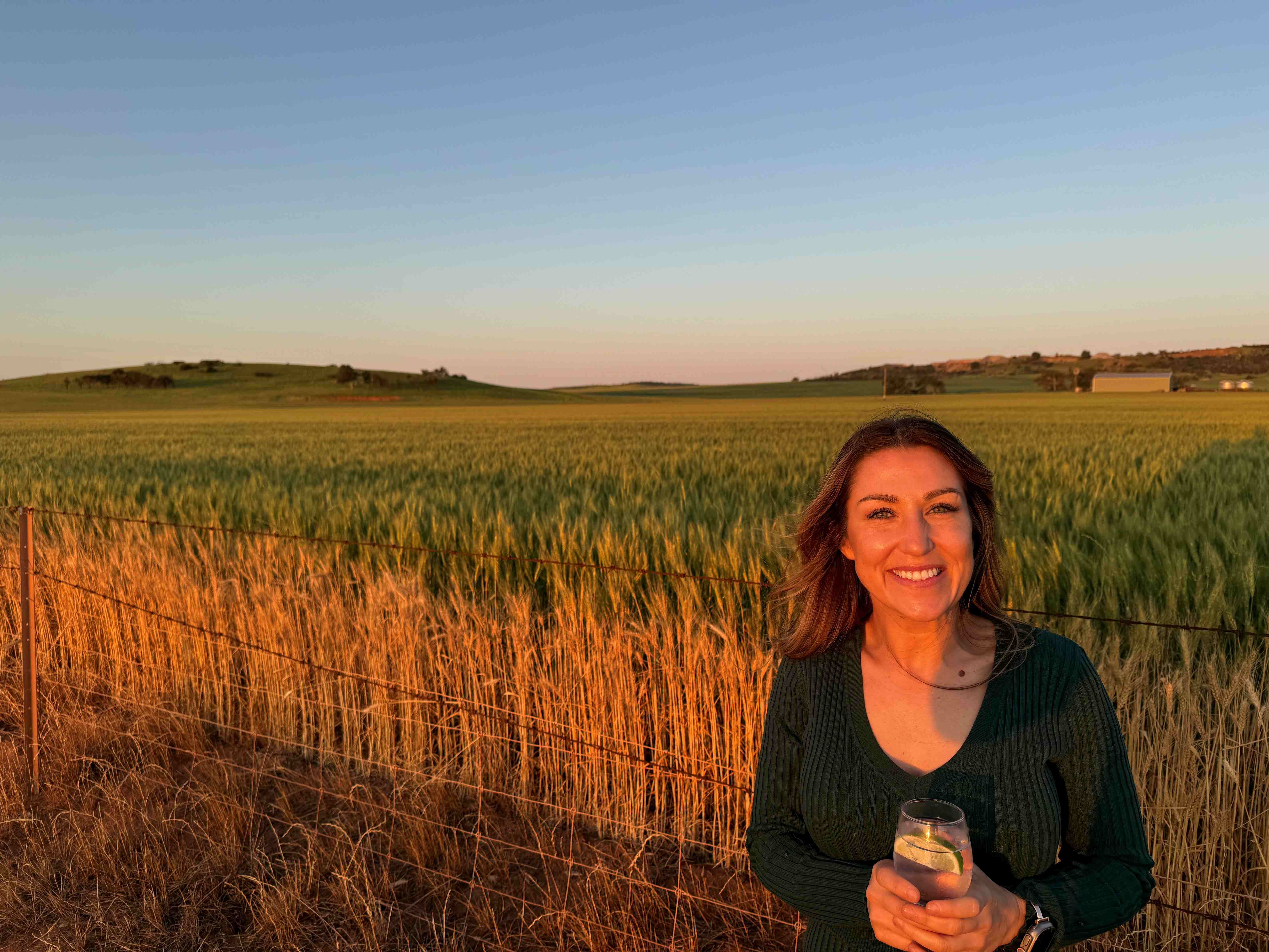 A woman standing in front of a crop holding a glass.