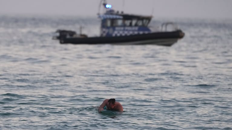 A surfer paddles back to shore as a police boat patrols the water after a reported shooting at Bondi Beach in Sydney