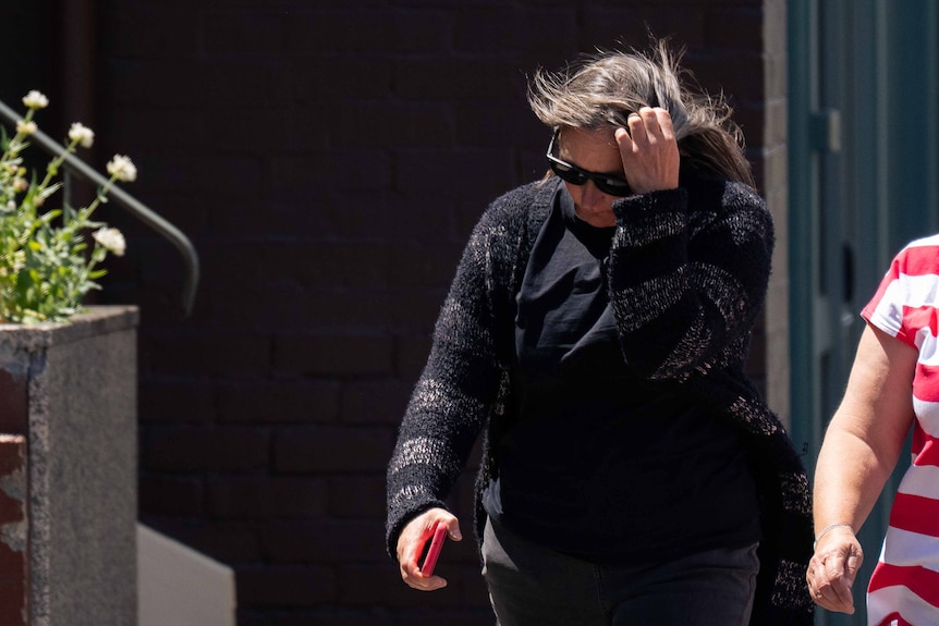 Two women walk towards a court, one hides her face with her hand.