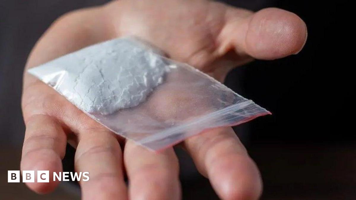 A hand with its fingers outstretched with a small bag of white powder on the palm.