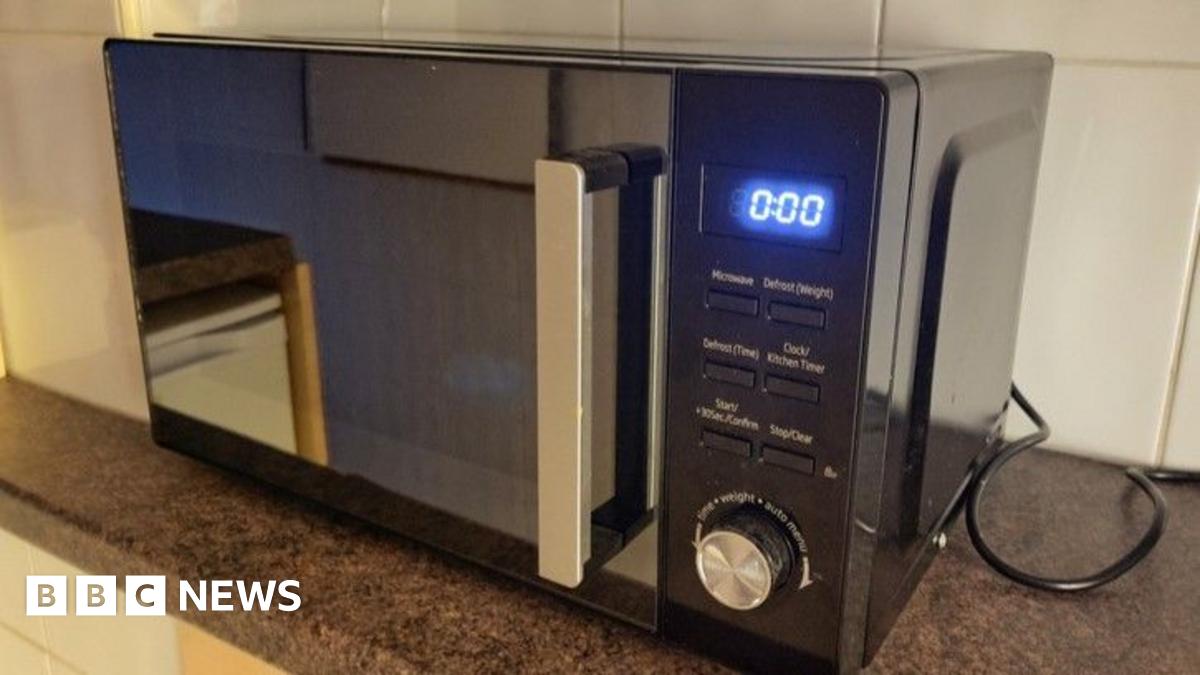 Close-up image of microwave oven on a worktop. It has a digital display, reading "0:00", six buttons, a dial and a mirrored door.