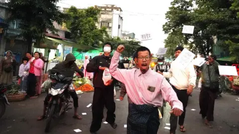 Tayzar San/Facebook Tayzar San distributing the leaflets boycotting the election, along with others on a busy street.