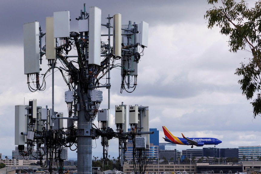 A blue, red and yellow Southwest plane landing behind a tall, white mobile connection tower