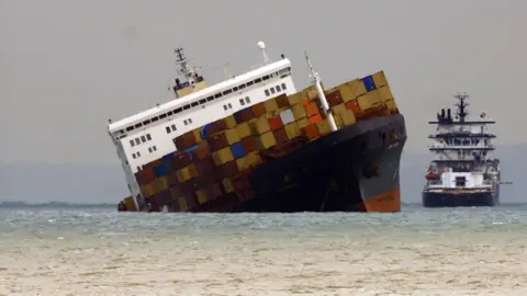 PA Media The Napoli lists heavily with containers on the deck and a tug off it's side