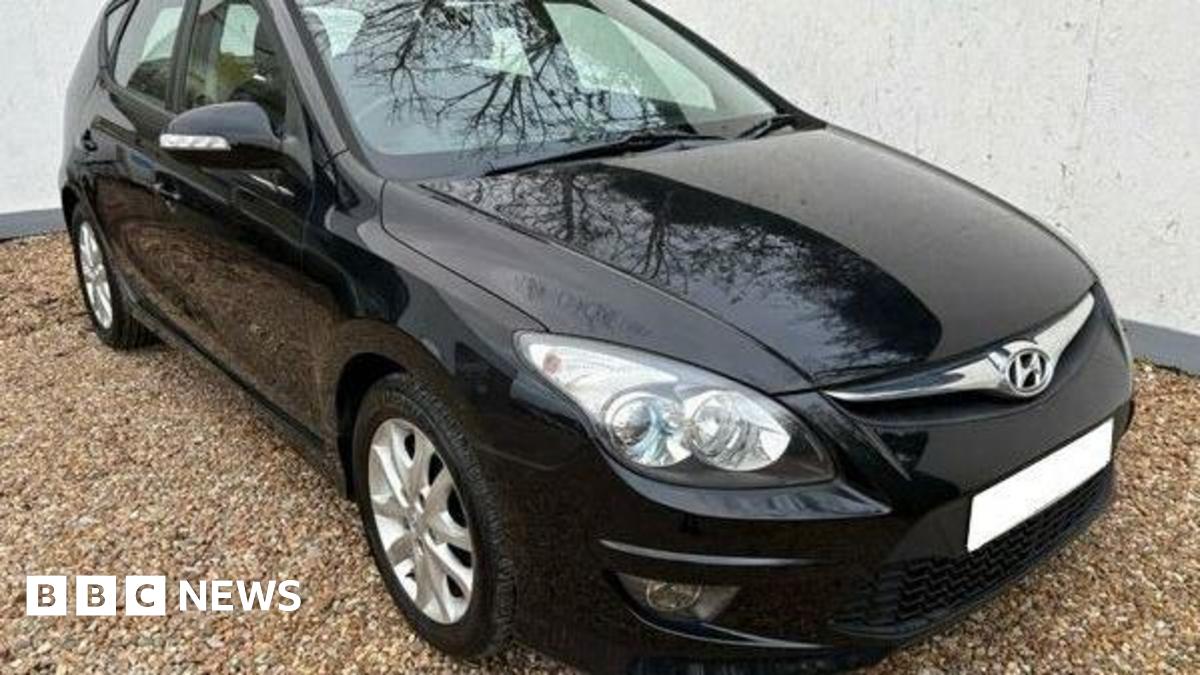 A black Hyundai i30 car with the registration plate blurred out  is parked on light-coloured gravel.