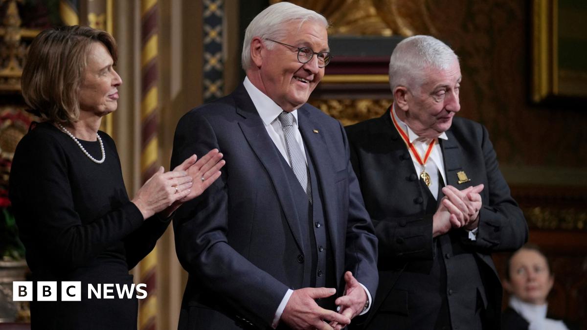 Claire Corkery, a woman with long hair, wearing a beige jumper and a gold necklace, standing in her dining room.