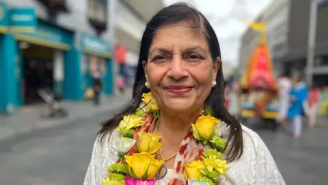 BBC Manjula Sood stood in a city street. She has long dark hair and is wearing a necklace made of flowers.