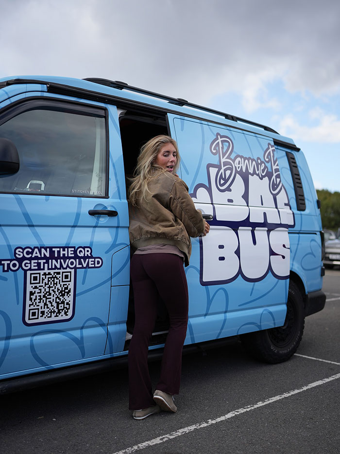 Woman opening door of a blue Bonnie Blue Bus with a QR code to get involved on a cloudy day in a parking lot