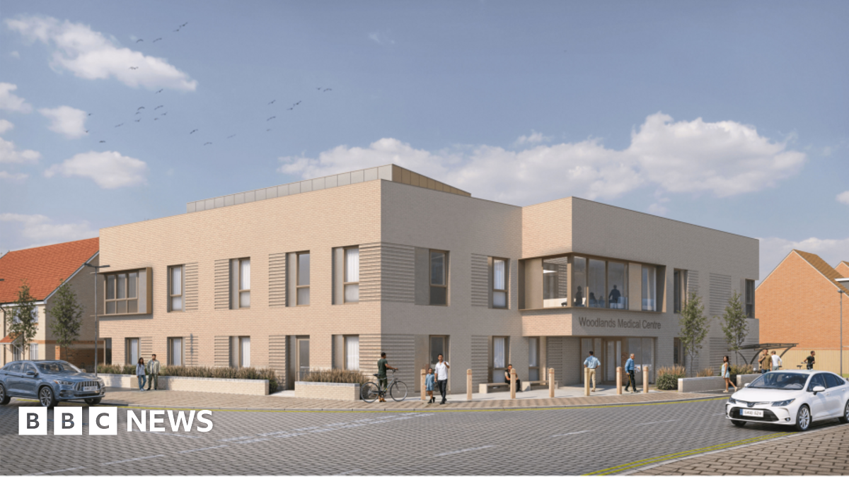 An artist's impression shows what the new GP surgery will look like. It is on the corner of two roads, and is a beige building with large windows. It says "Woodlands Medical Centre" on one side.