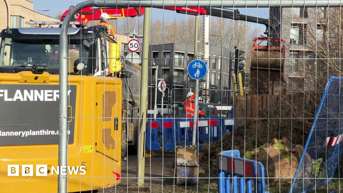 Metal fencing with machinery behind and plastic fencing with worker in orange high vis and white helmet.