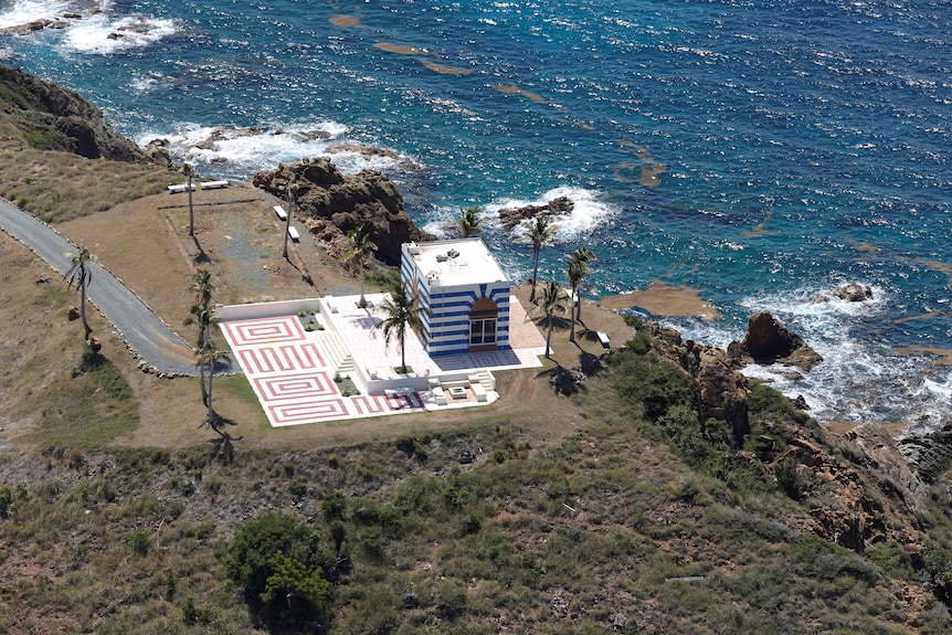 aerial view of a blue and white striped building next to a patterned tiled floor on a cliff