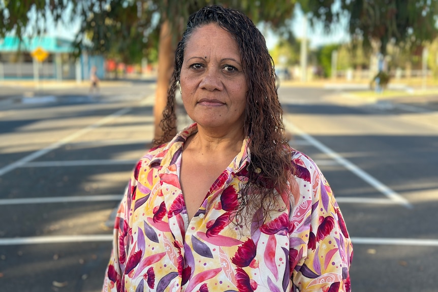 A woman with black curly hair looks at a camera