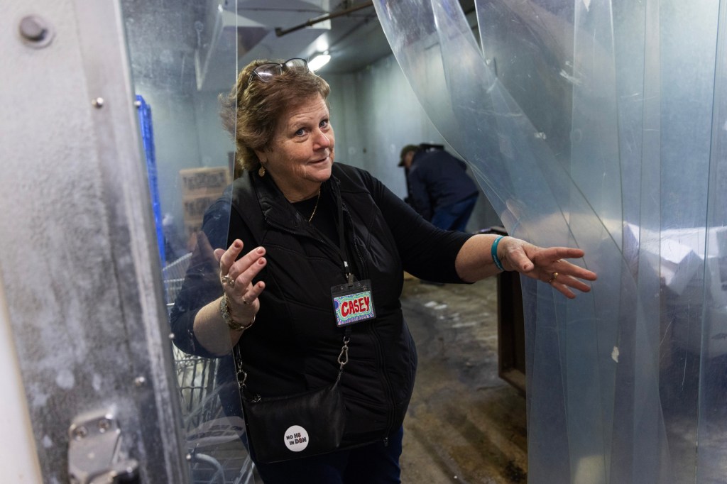 A woman pulls back a freezer curtain in the backroom of a grocery store.