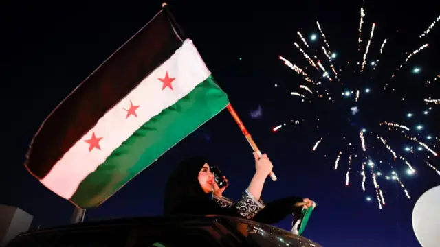 A woman holds up the flag adopted by the new Syrian rulers, as people celebrate after fighters of the ruling Syrian body ousted Syria's Bashar al-Assad, in the Damascus old city, Syria
