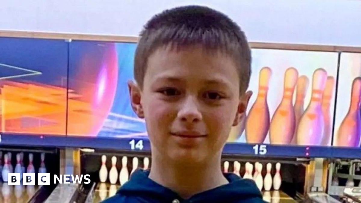 A young boy standing in a bowling alley with brown hair, smiling at the camera