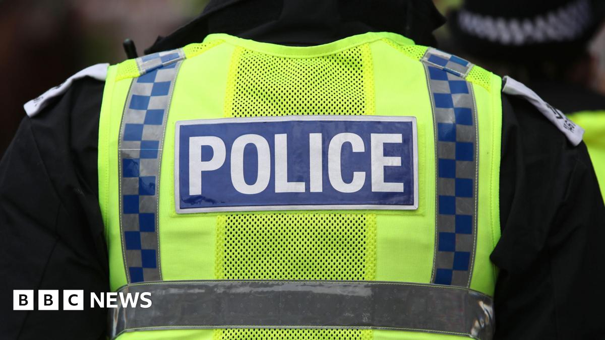 The back of a police vest. It is neon yellow and has two vertical stripes in navy and grey chequers. A navy blue rectangle says "police" in white lettering.