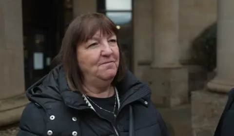 Carol Robertson, a woman with shoulder-length brown hair and a black puffer jacket stands outside a court building