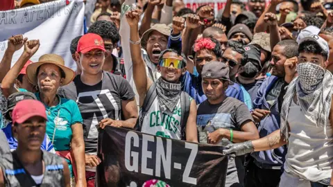 AFP via Getty Images A group of protesters, some holding up a 'Gen Z' banner punch the air with their fists.