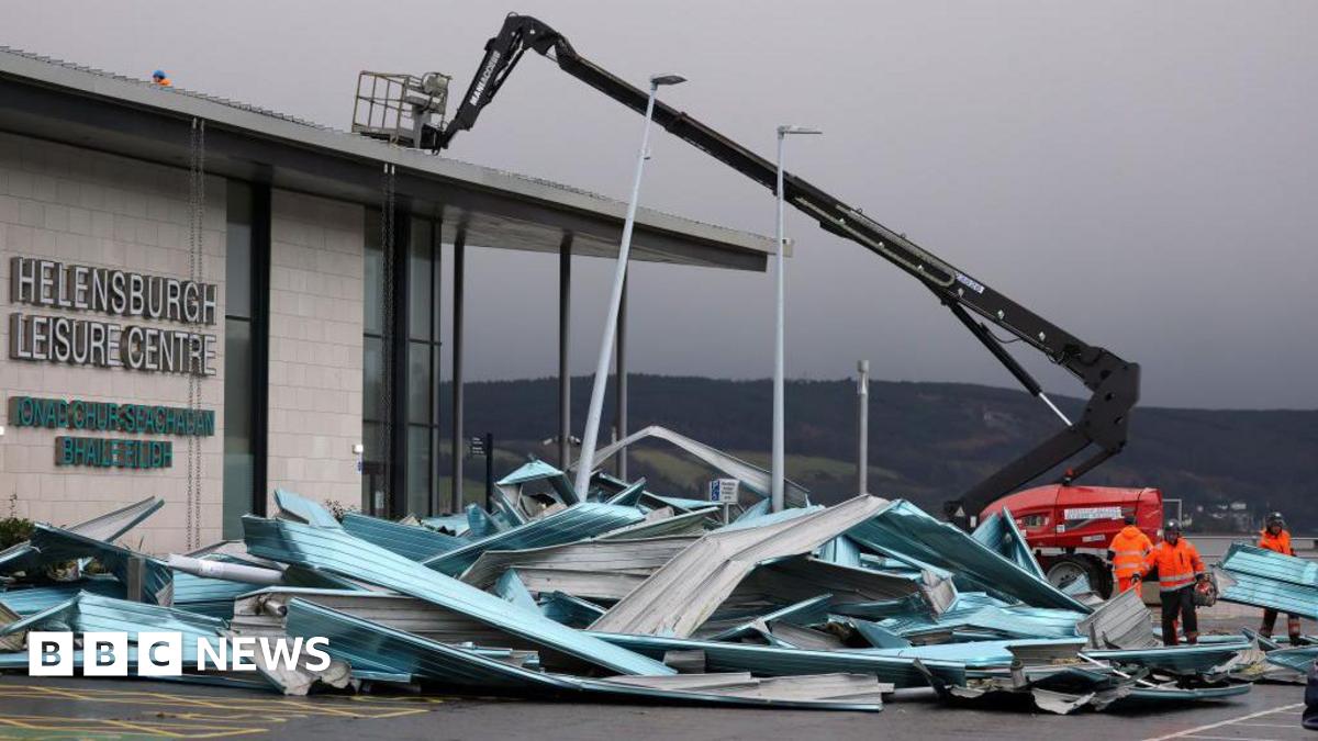 A crane carries out repair work on Helensburgh Leisure Centre - a large building with parts of the roof lying next to it, having been damaged by a storm.