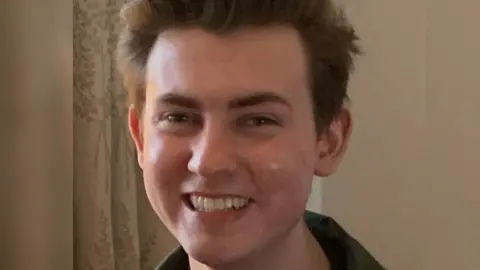 Aamer Anwar and Company Ethan Scott Brown,  young man with dark hair, is looking at the camera and smiling.