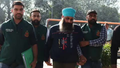 Getty A man with a blue turban is held by police