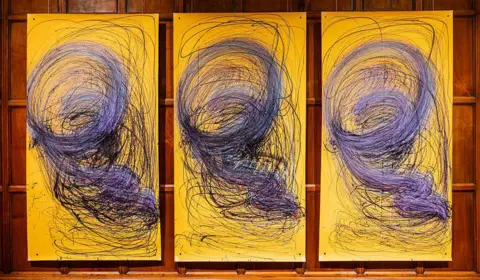 Getty Images Three large yellow paintings by Nnena Kalu in in a row with identical blue and black swirly patterns 