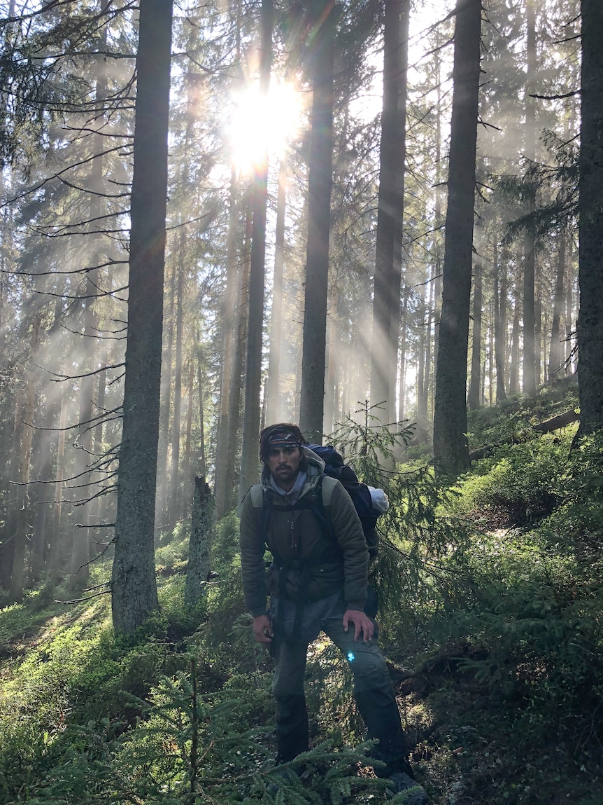A young man walking through a forest with sunlight streaming through the trees.