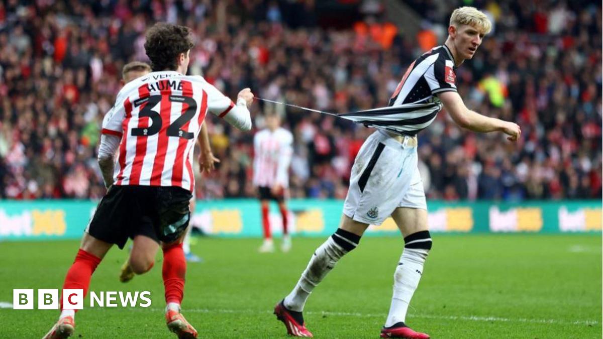 An action shot during Sunderland v Newcastle United in the 2024 FA Cup third round. Sunderland full back Trai Hume, wearing a red and white striped shirt with the number 32, has his back to the camera. In his right had he holds little more than a thread of winger Anthony Gordon's black and white striped shirt. That thread is tearing from the bottom of Gordon's shirt as he moves away from Hume. Other players and a section of crowd at the Stadium of Light are blurred in the background.
