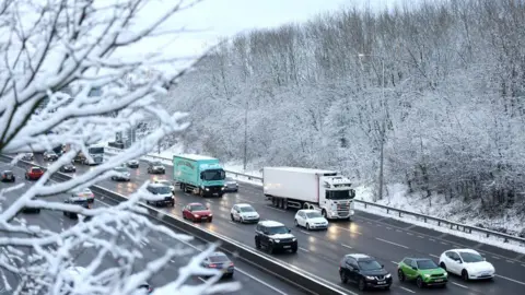Getty Images Cars and lorries travel along the M62 near Bradford on a wintry day. Headlights reflect on the wet carriageway and the picture is framed by snow-covered branches. 