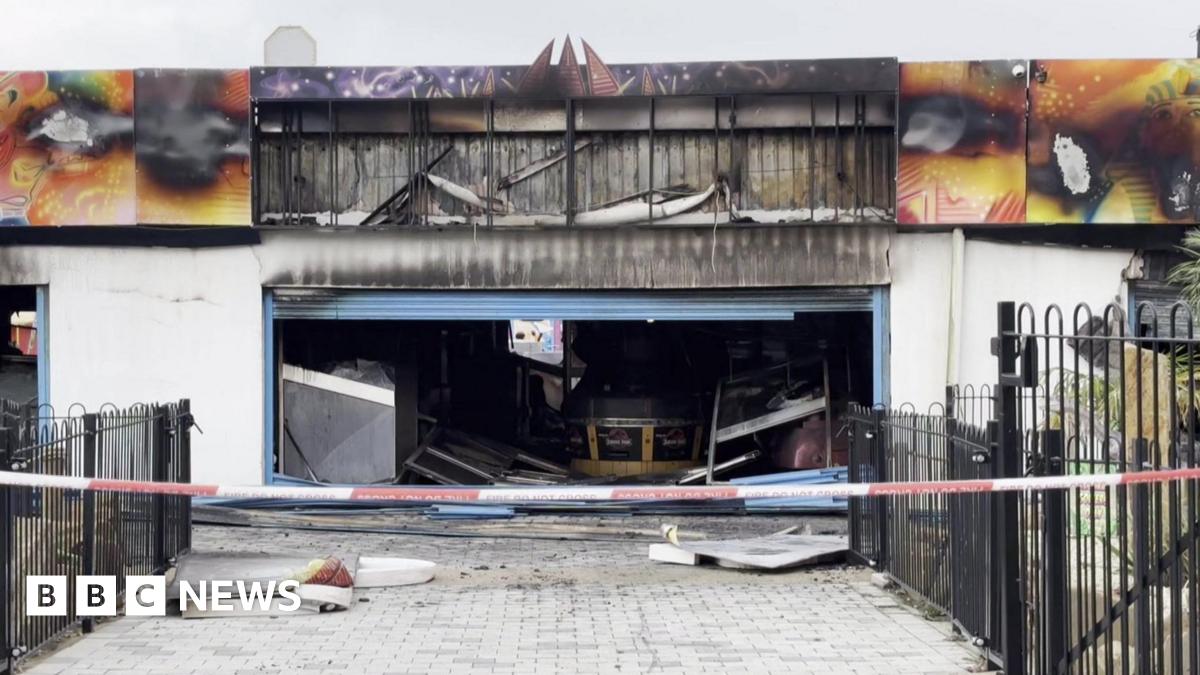 The arcade at Ocean Beach Pleasure Park after the fire. The metal shutters are open and show damage inside the building. Sheets of metal have fallen to the floor. Red and white no entry tape has been hung across the entrance.