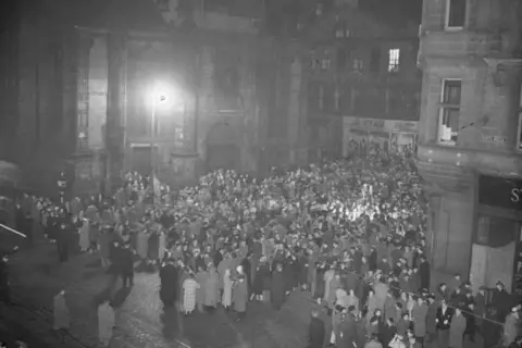 The Scotsman A black and white photograph of crowds standing at the foot of the Tron Church in Edinburgh.