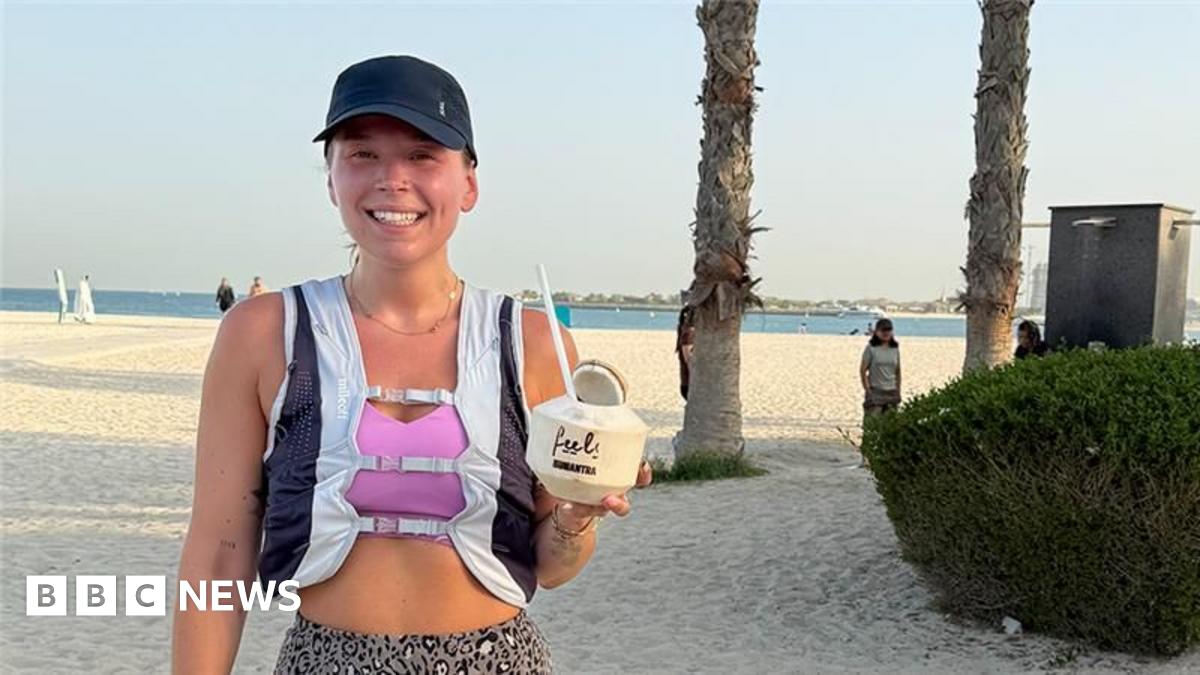 Sol Hyde takes a selfie. He is sitting on a bench with his laptop. He is wearing a black T-shirt, khaki trousers and white trainers. He has white earphones in. There are autumn leaves on the ground and a number of Lime hire bikes behind him.
