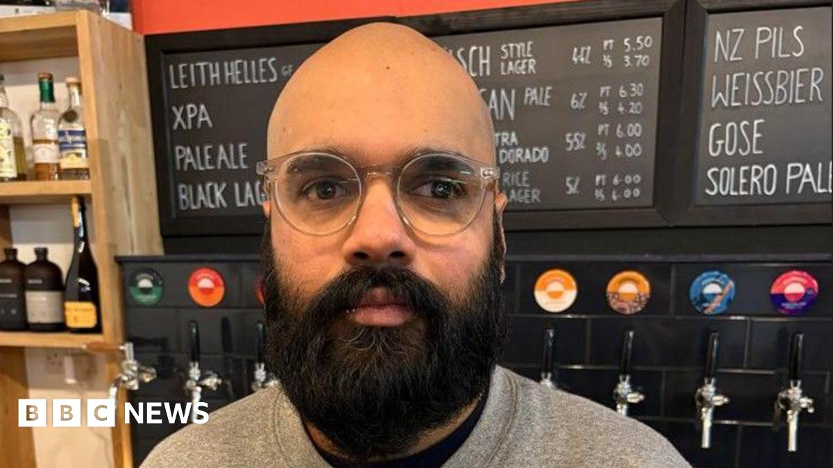 Head and shoulders image of Vinny Rosario looking straight at the camera. He is bald with a thick dark beard and moustache. He is wearing a grey sweatshirt and standing in front of a wall with lots of different coloured beer taps on it.