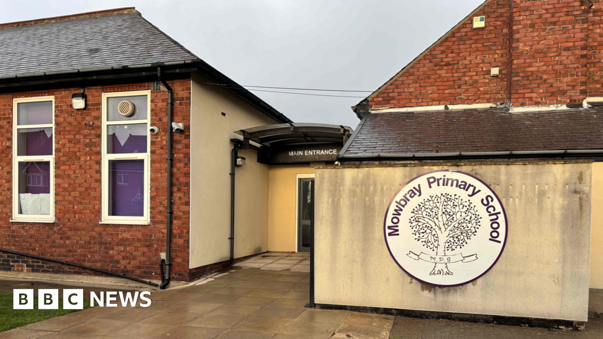 The outside of a one storey primary school with black fencing running around the outside of the building. Solar panels are attached to the roof.