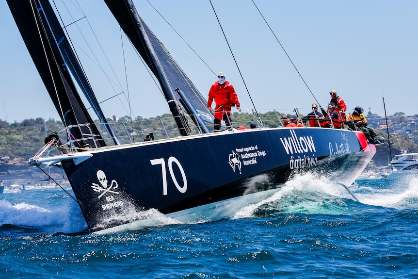 A person wearing a red sailing suit stands on a black yacht as it sails through the ocean.